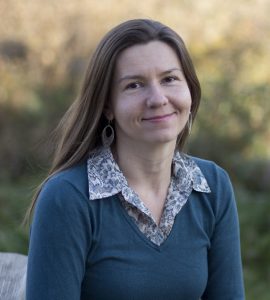 photo of Dagmara Antkiewicz wearing a dark green v-neck sweater over a green and white floral button down shirt.