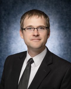 Photo of Rick Christensen wearing a dark suit and tie and a white button down shirt